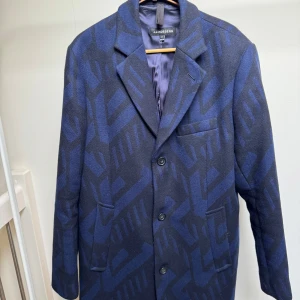 Blå mönstrad kavaj från J.Lindeberg - Säljer en snygg blå kavaj från J.Lindeberg med geometriskt mönster i mörkblått. Kavajen har klassisk krage, tre knappar framtill och tre fickor. Fodrad insida och tillverkad i ullblandning. Perfekt för dig som vill sticka ut med stil.
