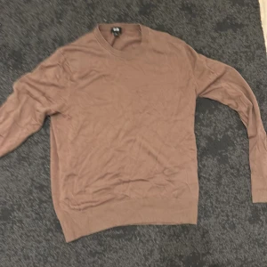 Beige stickad tröja från Uniqlo XS - En enkel och snygg beige stickad tröja från Uniqlo i storlek XS. Tröjan har rund hals och långa ärmar, perfekt för lager på lager. Materialet är mjukt och lätt, vilket gör den skön att bära under höst och vår. Passar dig som gillar stilrena och neutrala färger.
