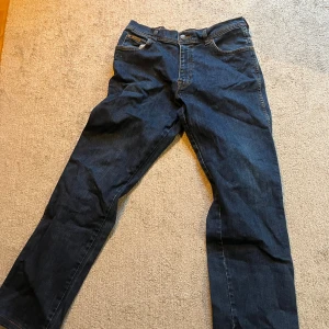 Gamla Wrangler jeans W33 L34 - Säljer ett par klassiska Wrangler Texas Stretch jeans i mörkblå färg, fick dem från farfar. De har raka ben, fem fickor och snygga kontrastsömmar. Materialet är stretchig denim som ger skön passform. Bakfickorna har den ikoniska Wrangler-loggan i läder. Benöppning rakt över 21 cm, midjan 40, benet 103 cm