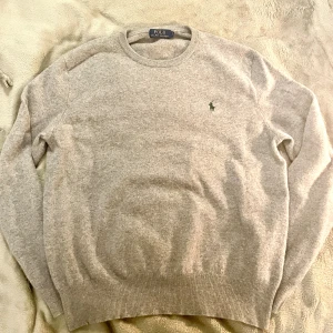Grå merinoulltröja Polo Ralph Lauren - Snygg grå tröja från Polo Ralph Lauren i 100% merinoull. Klassisk rund hals och långärmad modell med diskret broderad logga på bröstet. Perfekt för dig som gillar stilrena och mjuka plagg med premiumkänsla.