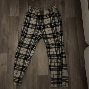 Julbyxor - Snygga rutiga byxor från Jack & Jones i svart, grått och beige. Byxorna har elastisk midja och avslappnad passform, perfekta för en chill och trendig look. Tillverkade i mjukt bomullsmaterial för extra komfort.