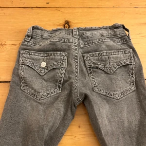 Grå bootcut jeans från Gina Tricot - OBS! En knapp har lossnat från bakfickan!!Snygga grå jeans från Gina Tricot i storlek 158. Modellen har bootcut-ben och coola bakfickor med flätad kant och knappdetalj. Jeansen har klassisk femficksdesign och är tillverkade i mjukt denimtyg som sitter skönt.