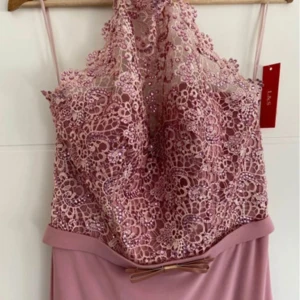 Rosa långklänning med spets och rosett - Säljer en elegant rosa långklänning från L&S med smala axelband och vacker spets upptill dekorerad med små pärlor. Klänningen har en söt rosett i midjan och ett slätt, mjukt tyg nedtill. Perfekt för dig som vill sticka ut med en romantisk look.