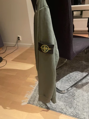 Stone Island grön sweatshirt - Säljer en grön crewneck från Stone Island med den klassiska patchen på vänster ärm. Tröjan har rund hals, ribbade muddar och är tillverkad i mjuk bomull. Perfekt för dig som gillar streetwear och vill ha något stilrent med ikonisk detalj.