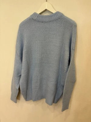 Ljusblå stickad tröja med rund hals - Mysig ljusblå stickad tröja från lager 157 med rund hals och ribbade muddar vid ärmslut och nederkant. Tröjan har en loose passform och är perfekt för kyliga dagar. Enkel och stilren design som är lätt att matcha med jeans eller kjol.