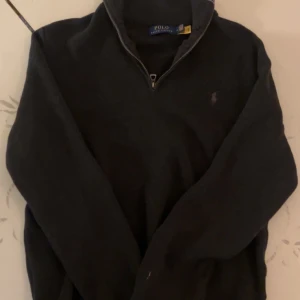 Svart half zip tröja Polo Ralph Lauren - Svart långärmad tröja från Polo Ralph Lauren med half zip och klassisk krage. Diskret broderad logga på bröstet. Tröjan är i stickad bomull och har en clean, normal passform som funkar till många olika stilar.