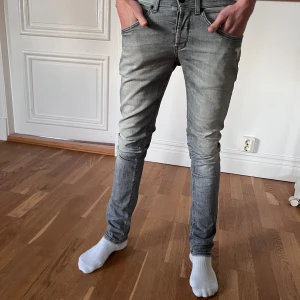 Dondup George  - Säljer ett par grå dondup jeans med slitning vid fickan. Jeansen har klassisk femficksdesign, smal passform och normal midja. Perfekta för dig som gillar en tajt look och vill ha ett par stilrena jeans i garderoben.