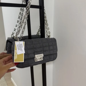  Michael Kors - Snygg grå quiltad axelväska från Michael Kors med silverfärgad kedjerem och metallspänne framtill. Helt ny oanvänd. Nypris 3500 kr.