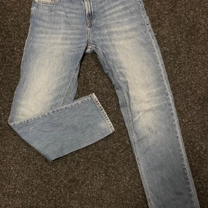 Blå jeans Jack & Jones - Snygga blå jeans från Jack & Jones i storlek 176, med klassisk femficksdesign och raka ben. Jeansen har ljus tvätt och kontrastsömmar, vilket ger en cool och tidlös look. Perfekta för dig som gillar enkel och stilren denim. Har ett litet märke på högra benet men inget man lägger märke till.