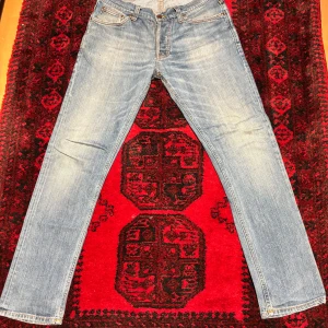 Ljusblå jeans från Nudie Jeans - Säljer ett par ljusblå jeans från Nudie Jeans med klassisk femficksdesign och snygga kontrastsömmar. Jeansen har rak passform och är tillverkade i mjukt jeanstyg. Bakfickorna har Nudie Jeans signaturbroderi. Perfekt för dig som gillar stilrena och tidlösa jeans.