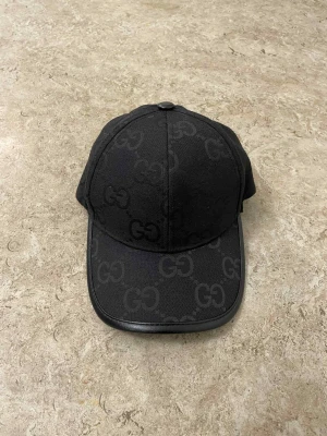 Svart GG-mönstrad keps från Gucci - Snygg svart keps från Gucci med GG-logga som mönster över hela kepsen. Kepsen har böjd skärm med läderkant och justerbart spänne bak i svart läder. Perfekt för dig som gillar exklusiva accessoarer med stilren design.