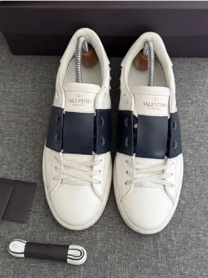 Valentino Open mörk Blå 40-41 - Snygga Valentino Garavani Open sneakers i storlek 40 men kan passa 41  i vitt skinn med bred mörkblå rem över mitten. Klassisk rund tå, platt sula och vita snören. Nyskick! Tar byten.