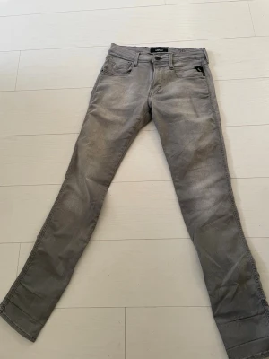 Replay Anbass grå jeans, storlek 29 waist  - Snygga Replay Anbass jeans i en ljusgrå tvätt med klassisk femficksdesign och smal passform. Jeansen har låg midja och är tillverkade i mjukt stretchigt bomullsmaterial för extra komfort. Perfekt för dig som gillar stilrena och moderna jeans. 29 W 32L