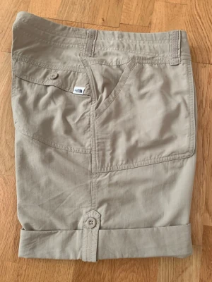 Beige shorts från The North Face - Snygga beige shorts från The North Face med praktiska fickor och knappdetaljer vid benslut. De har midwaist passform och är gjorda i lätt och slitstarkt material, perfekt för varma dagar.