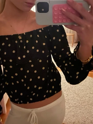 Svart offshoulder prickig topp - Säljer en svart offshoulder topp med guldiga prickar. Toppen har långa ärmar och resår vid axlar och midja för en snygg passform. Jättesnygg och knappt använd! 