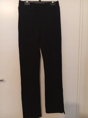 Svarta raka byxor i kostym från Lindex  - Svarta raka byxor i kostym från Lindex i storlek XS. Byxorna har en slits vid benslutet och är tillverkade i ett mjukt och tjockt material som känns skönt mot huden. De har en enkel design med elastisk midja och passar perfekt för dig som gillar stilrena och bekväma plagg. Inte använd en ända gång helt ny.