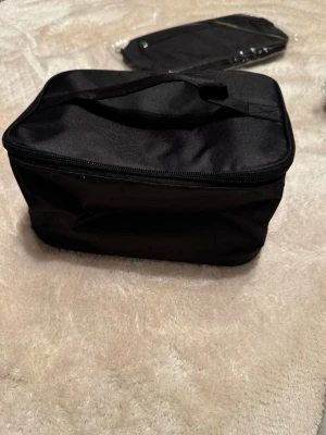 Svart necessär med dragkedja - Praktisk svart necessär med handtag på ovansidan och dragkedja runt om. Insidan har ett stort fack och ett meshfack med dragkedja i locket. Perfekt för att organisera dina grejer när du är på språng.