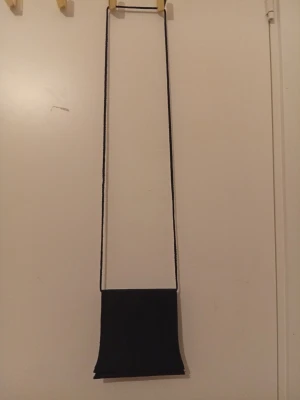 Svart axelväska med struktur - Säljer en svart axelväska med lång axelrem och ett handtag som kan knäppas av med tryckknappar. Väskan har en stilren, rektangulär form och är gjord i ett tyg med diskret strukturerad yta. Perfekt för dig som gillar minimalistisk design och vill ha en väska som sticker ut lite.