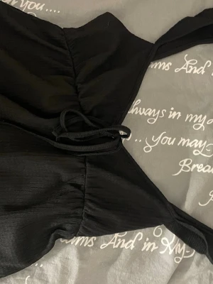 Svart omlott topp från Nelly XXS - Säljer en svart omlott topp från Nelly i storlek XXS. Toppen har breda axelband och snygg snörning framtill som ger en cool look. Materialet är mjukt. Perfekt att styla med jeans eller kjol för en trendig outfit. 💕