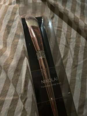 Nikolai foundationborste - Foundationborste från Nikolai med roséguldfärgat handtag med strass på. Borsten har täta, vita syntetiska strån och är vegansk, cruelty free och ej testad på djur💕