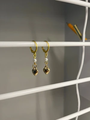 Örhängen  -  Ett par guldfärgade örhängen med guldiga, plasthjärtan och vita pärlor men resten är i rostfritt stål och handgjorda 