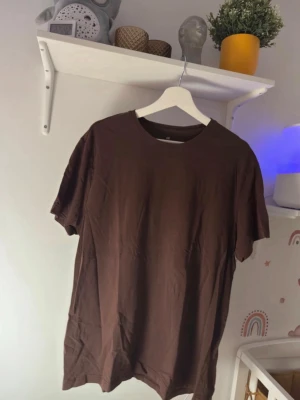 Brun basic t-shirt från H&M - En enkel brun t-shirt från H&M med rund halsringning och korta ärmar. Tillverkad i mjuk bomull för en skön känsla. Perfekt till jeans eller shorts för en clean och avslappnad look.