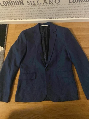 Mörkblå kavaj från H&M strl 164 - Snygg mörkblå kavaj från H&M i storlek 164. Klassisk modell med två fickor framtill, knäppning med en knapp och helfodrad insida. Perfekt för dig som vill ha en stilren look med enkel passform och diskret struktur i tyget. För ENDAST 400kr så får du en nästan oanvänd kavaj som är perfekt för barn för speciella tider.