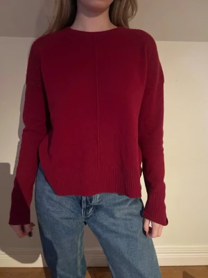 Mörkröd stickad tröja med struktur - Snygg mörkröd stickad tröja med rund hals och ribbade detaljer på axlar och muddar. Tröjan har en rak passform och långärmade ärmar, perfekt att matcha med jeans. Enkel design med en diskret söm framtill som ger lite edge.