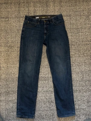 Lee Slim Fit MVP jeans blå W32 L32 - Snygga mörkblå jeans från Lee i modellen Slim Fit MVP. Klassisk femficksdesign med Lee-läderpatch bak i midjan. Jeansen har en smal passform och är tillverkade i stretchig bomull för extra komfort. Perfekta för dig som gillar stilrena och bekväma jeans.