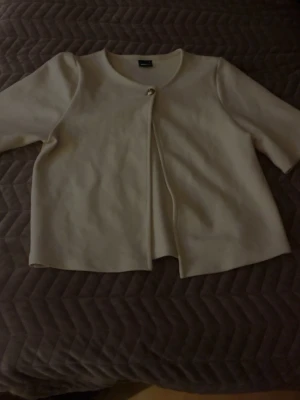 Beige kofta från Gina Tricot - Säljer en stilren beige kofta från Gina Tricot i storlek S. Koftan har rund halsringning, trekvartsärmar och stängs med en dekorativ knapp framtill. Materialet är mjukt och har en lätt struktur som ger en clean look. Fråga gärna om fler bilder 🥰