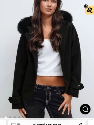 Svart kappa med fuskpäls från Gina Tricot - Stilren svart kappa med huva och mjuk fuskpäls runt kanten. Jackan har knappar vid ärmslut och framtill, samt en rak och lite boxig passform. Perfekt för dig som vill ha en snygg och mysig look under höst och vinter.