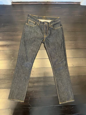 Nudie Jeans Grim Tim dry navy - Säljer ett par Nudie Jeans Grim Tim i färgen org. dry navy. Klassisk femficksmodell med kontrastsömmar och rak passform. Tillverkade av 99% ekologisk bomull och 1% elastan för lite stretch. Snyggt läderpatch bak i midjan och stilrena detaljer.