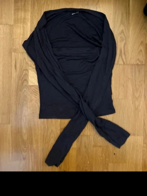 Mörkgrå omlott bolerotopp Gina Tricot - Säljer en svart bolerotopp från Gina Tricot i storlek S. Toppen har omlott-design med långa ärmar och är gjord i mjuk bomull. Tröjan har slits vid ärmarna 