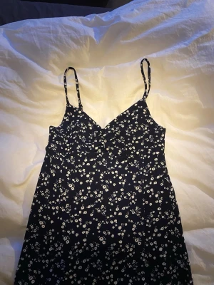 Mörkblå blommig sommarklänning - Supersöt mörkblå klänning från Gina med vita småblommor och smala axelband. Klänningen har en v-ringad omlottliknande överdel och är perfekt för varma dagar. Lätt och luftig modell som ger en avslappnad vibe. Jag som är 177cm lång så går den ner till mitten av smalbenet. Endast använd vid ett tillfälle så i superskick.