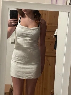 Vit kort klänning med tunna axelband - Säljer en vit kort klänning med tunna axelband och subtilt blommönster. Klänningen har en smickrande passform och lätt draperad urringning. Perfekt för sommarens alla tillfällen!