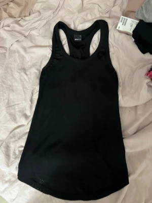 Svart linnetopp från Stronger - Snygg svart linnetopp från Stronger med brottarrygg och ventilerande meshdetaljer på sidorna. Perfekt för dig som gillar en sportig och enkel stil. Tillverkad i mjukt och stretchigt material som passar till träning eller chill.