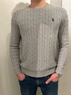 Grå kabelstickad tröja Polo Ralph Lauren - Snygg grå kabelstickad tröja från Polo Ralph Lauren. Tröjan har långa ärmar och ribbade muddar vid ärmslut och nederkant. Perfekt till jeans för en clean look. Storlek S. Priset kan diskuteras