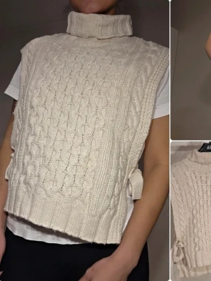 Stickad väst med polokrage från MSCH - Krämvit stickad väst från MSCH med polokrage och snyggt flätmönster framtill. Västen har knytband i sidorna och ribbade kanter. Perfekt att slänga över en t-shirt eller skjorta för en trendig lager-på-lager-look.