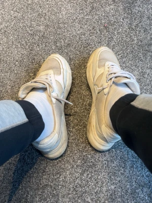 Vita axel arigato skor - Snygga stilrena sneakers i beige och vitt med meshdetaljer och tjock sula. Skorna har klassisk snörning och en modern, sportig look som passar till streetwear. Perfekta för dig som gillar stilrena men ändå trendiga sneakers. 