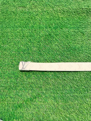 Louise Vuitton beige bälte med monogram - Stilrent beige bälte från Louise Vuitton med klassiskt L.V-monogram och silverfärgat L.V-spänne. Bältet har en elegant design och är tillverkat i skinn med subtila logodetaljer längs hela remmen.