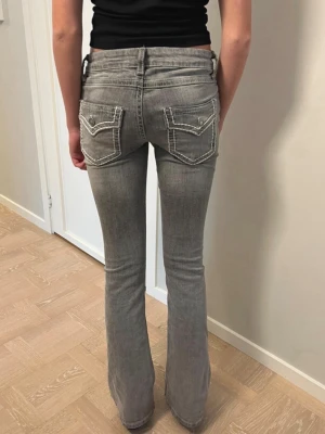 Jeans bootcut, low waist, Gina Tricot 164, XS - Lågmidjade utsvängda grå Jeans med vita detaljsömmar på bakfickorna och justerbar midja. De är bortsett från en liten fläck på vänster bakficka i väldigt fint skick. Inget slitage nertill.   Storlek 164, motsvarar XS Mått innerben 83 cm Mått över midjan 35 cm