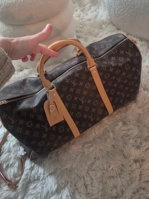 Louis Vuitton monogram resväska - Snygg resväska från Louis Vuitton i klassiskt brunt monogrammönster med ljusbruna läderdetaljer och guldfärgade metalldragkedjor. Perfekt för weekendresor och har en ikonisk design som sticker ut.