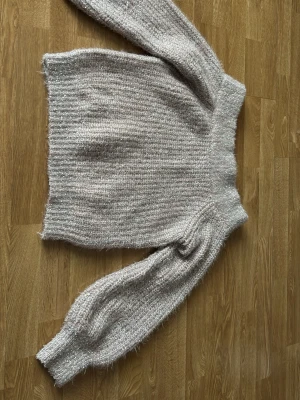 Glittrigljus /gammelrosa stickad tröja XS/S - Mysig stickad tröja i beige med inslag av silverglitter. Tröjan har lång ärm, ribbstickade muddar och en mjuk, fluffig känsla. Perfekt för dig som gillar lite extra shine i vardagen. Materialet känns lätt och stretchigt.