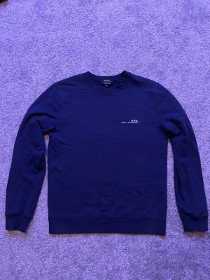 Mörkblå sweatshirt från A.P.C. - Mörkblå crewneck sweatshirt från A.P.C. med diskret vit logotyp på bröstet. Klassisk passform med ribbade muddar vid ärmslut och nederkant. Tillverkad i mjuk bomull för en clean och stilren look.        Köpt för 2500 säljer för 799, skriv gärna vid fundering. 