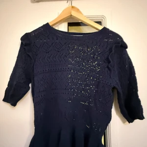 Mörkblå stickad tröja Holly & Whyte - Mörkblå stickad tröja från Holly & Whyte med snyggt hålmönster och rund halsringning. Tröjan har puffiga axlar och är tillverkad i ett mjukt material som känns skönt mot huden. Perfekt för dig som gillar stilrena och trendiga plagg.