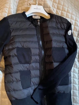 Äkta Svart pufferjacka från Moncler - Säljer en svart pufferjacka från Moncler som är äkta med quiltad front, fyra fickor och Moncler-logga på ärmen. Jackan har dragkedja framtill och är långärmad med en clean, stilren look. Perfekt för dig som vill ha något både snyggt och funktionellt. I storlek S. Priset kan förhandlas.