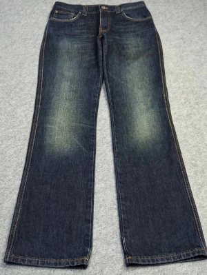 Mörkblå bootcut jeans från Nudie - Säljer ett par mörkblå bootcut jeans från Nudie med snygga slitningar framtill och klassiska kontrastsömmar. Jeansen har fem fickor och Nudie-logga på bakfickan. Tillverkade i kraftig denim som ger en schysst vintagekänsla.