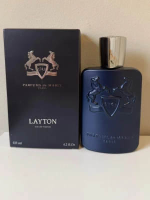 Parfums de Marly Layton EdP 125ml - Lyxig parfym från Parfums de Marly, Layton Eau de Parfum i en elegant mörkblå flaska med silverfärgad kork. Flaskan har en stilren design med två hästar i relief och märkets logotyp. Förpackningen är också mörkblå med silverdetaljer. Volym: 125 ml.