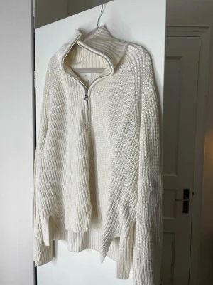 Vit ribbstickad halvzip-tröja - Säljer en vit ribbstickad tröja med halvzip och hög krage. Tröjan har långa ärmar och en avslappnad passform. Perfekt för lager på lager och enkel att styla till olika outfits.