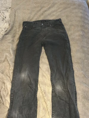 Gråa jeans från Armani Jeans - Säljer ett par gråa jeans från Armani Jeans med klassisk femficksmodell och raka ben. Jeansen har diskret logga på bakfickan och metallknapp framtill. Materialet är mjukt och bekvämt, perfekt för en avslappnad stil.